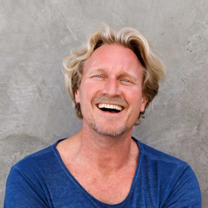 A man with blonde hair and blue shirt smiling.